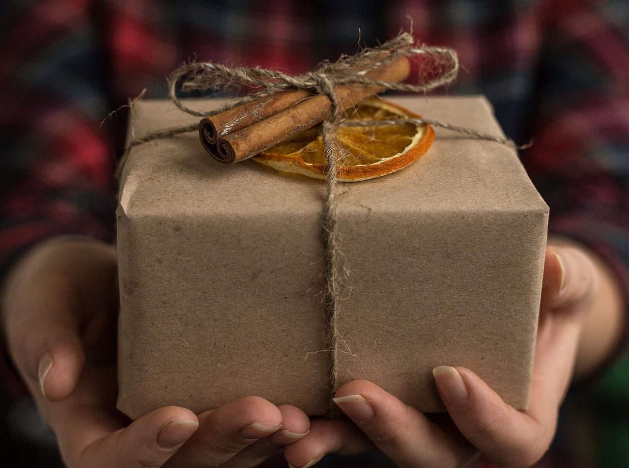 White hands holding a wrapped box, adorned with dried orange and a cinnamon stick